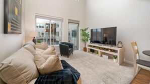 A modern living room with a large TV, comfortable seating, and a view of the city through large windows. - 3 Bedroom Centrally Located (Columbus)