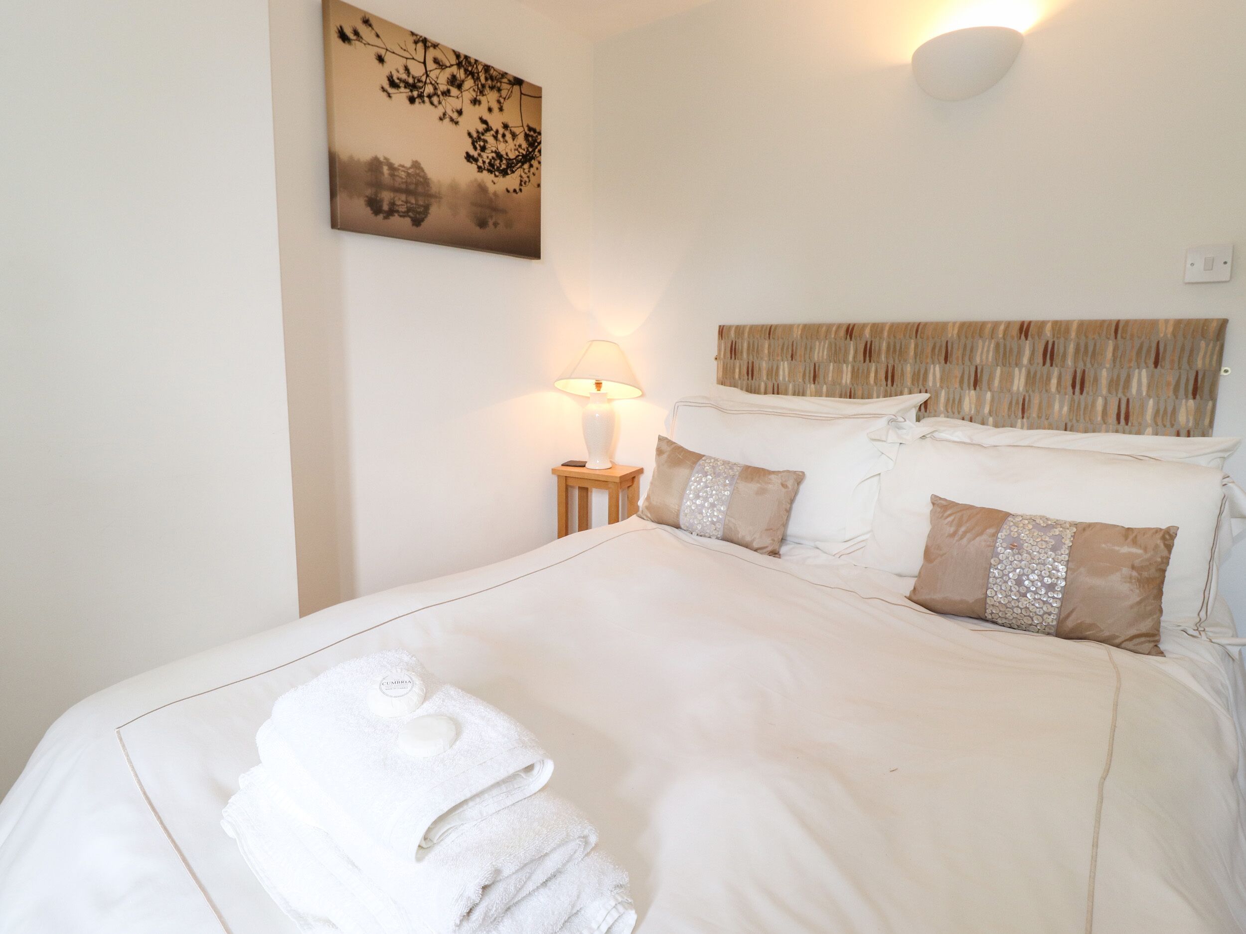 A neatly made bed with white linens and a set of folded towels.