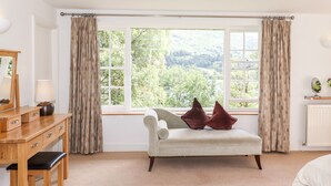 A room with a wooden desk, a white sofa with two pillows, a large window with curtains, and a radiator.