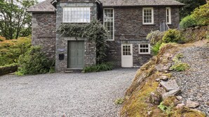 A stone house with a gravel driveway, a green door, and a stone staircase leading up to the entrance.