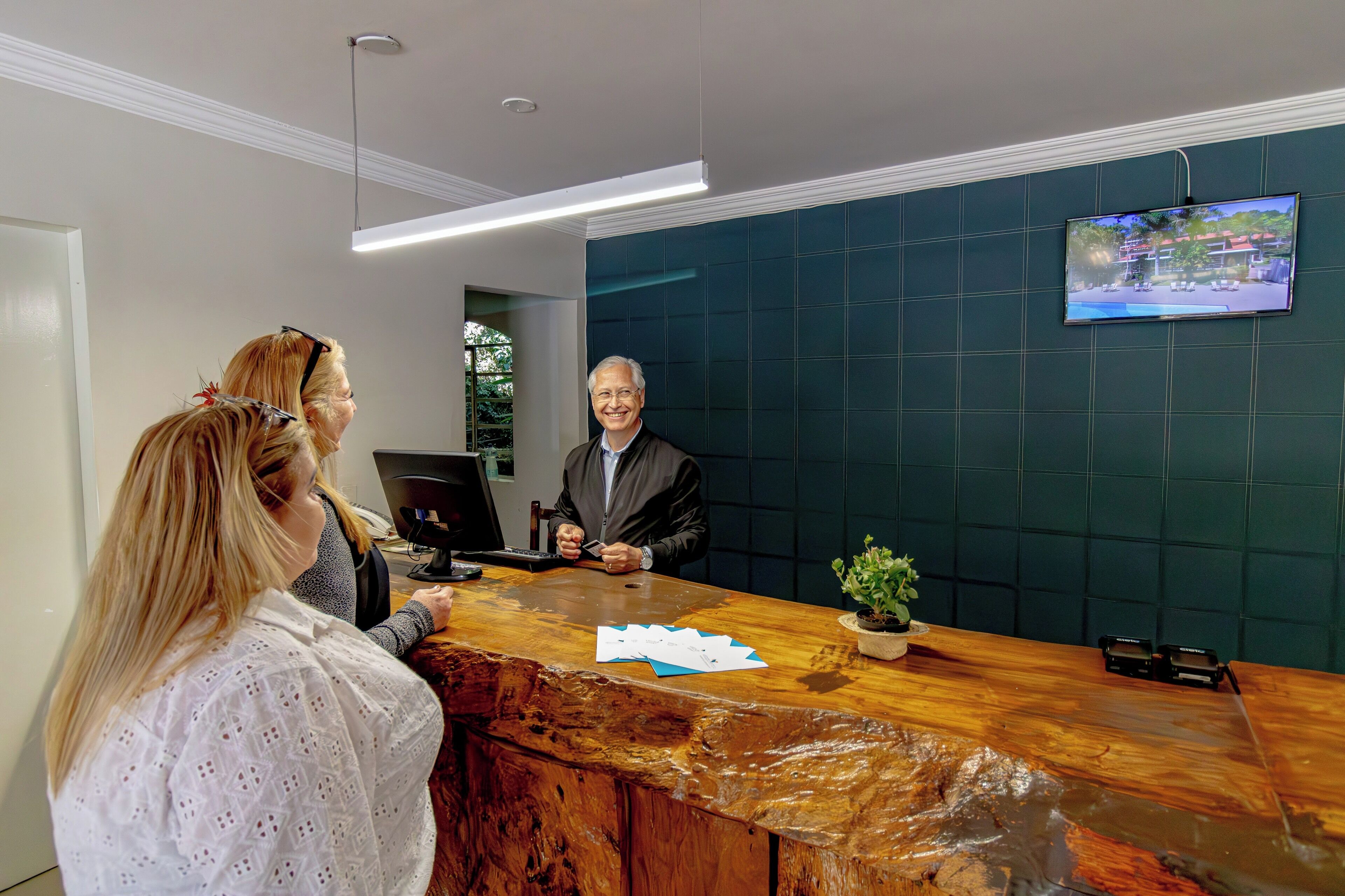 A reception desk with a wooden counter, a television mounted on the wall, and a potted plant.