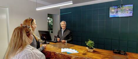 A reception desk with a wooden counter, a television mounted on the wall, and a potted plant.
