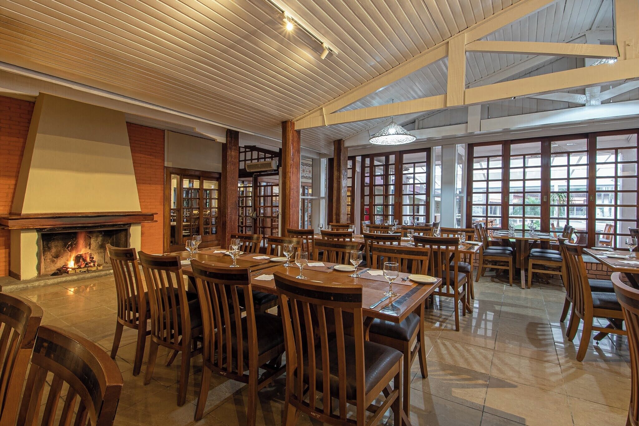 A restaurant with wooden tables and chairs, a fireplace, and large windows allowing natural light.