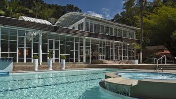 A swimming pool with clear water, a covered area with large windows, and a palm tree in the background.