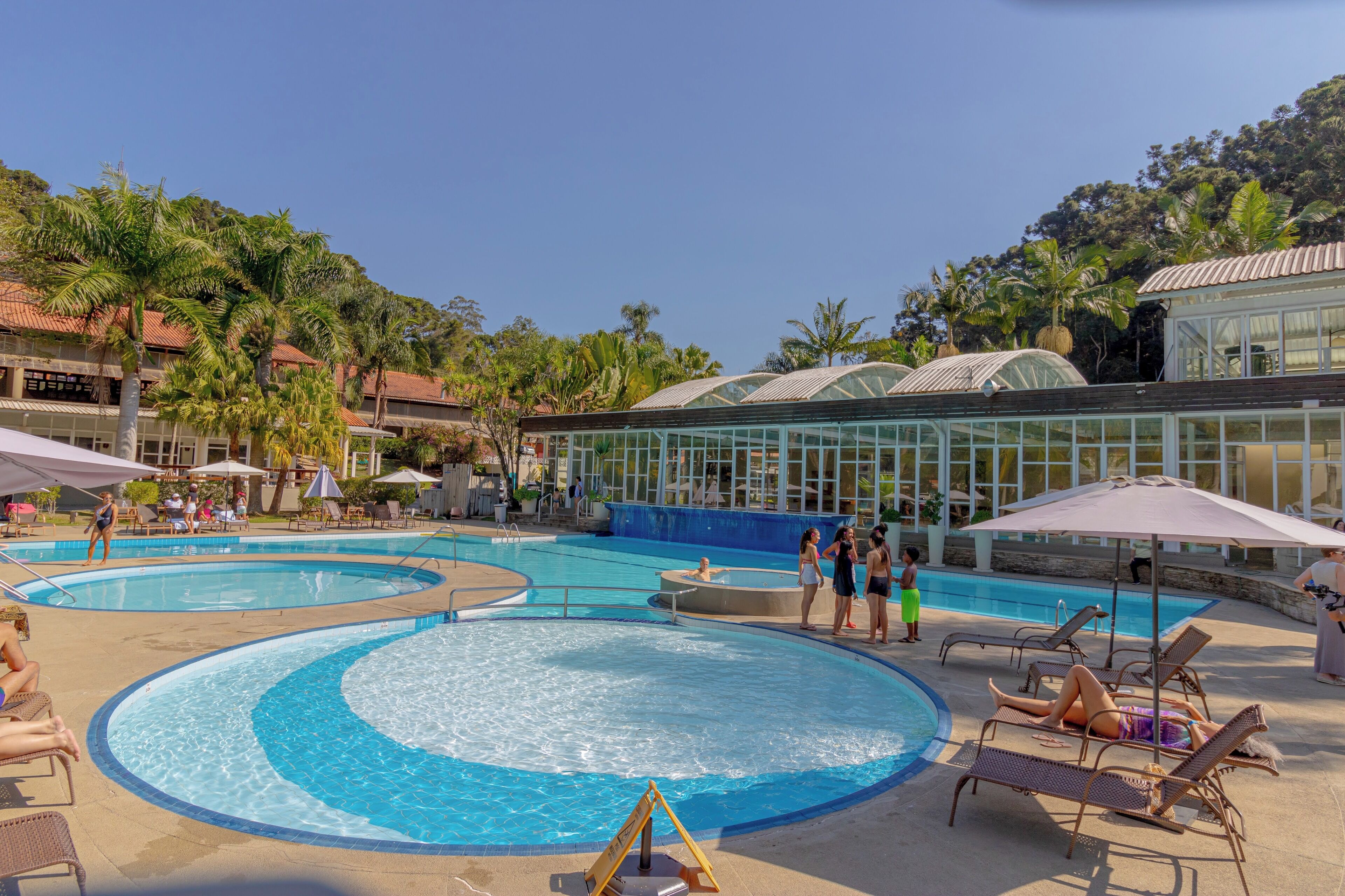 Un área de piscina con varias piscinas, sillas de descanso, sombrillas y palmeras.