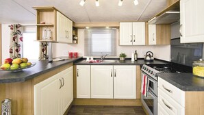 A compact kitchen with white cabinets, a black countertop, a stove, and a window with blinds.