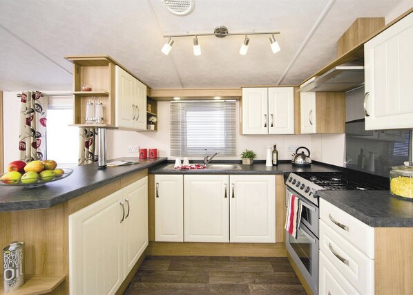 A compact kitchen with white cabinets, a black countertop, a stove, and a window with blinds.