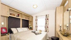 A bedroom with a bed, bedside tables, a dresser, a mirror, and a window with curtains.