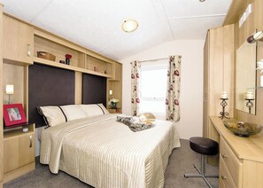 A bedroom with a bed, bedside tables, a dresser, a mirror, and a window with curtains.