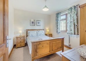 A bedroom with a wooden bed, two bedside tables with lamps, a window with floral curtains, and a radiator.