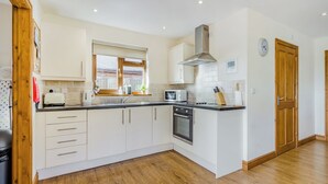 A modern kitchen with white cabinets, a built-in oven, a microwave, and a window with blinds. - Valley View Lodge Pet (Penybont, Llandrindod Wells)