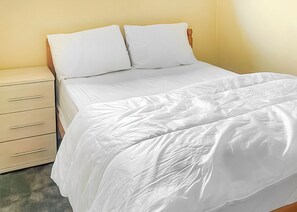 A bed with white bedding, a wooden headboard, and a beige nightstand with drawers. - Gold 2 Bedroom Chalet (Brixham, Torbay)
