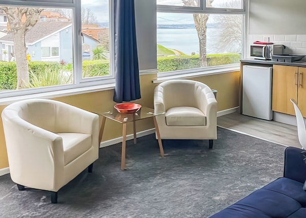 A modern living room with two armchairs, a small table, and a view of a body of water through large windows.