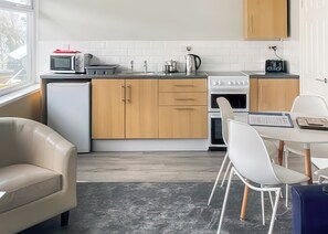 A modern kitchen with a refrigerator, microwave, stove, and sink. There is a dining area with a table and chairs.