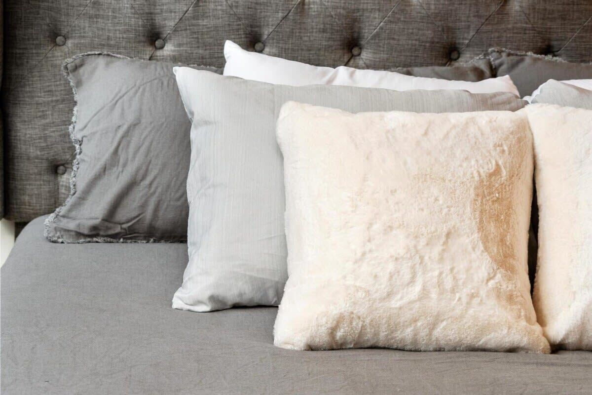 A bed with grey bedding and three pillows in shades of grey and white.