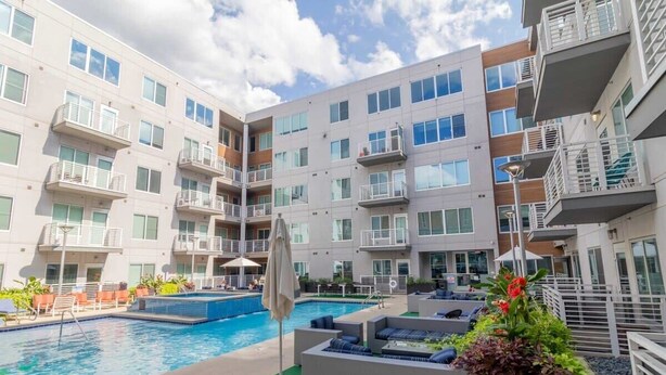 A modern multi-story hotel with a central swimming pool, outdoor seating, and balconies.