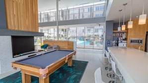 A modern indoor pool area with a pool table, bar seating, and a view of the pool.