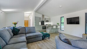 Een moderne woonkamer met een grijze hoekbank, een klein keukenhoekje en een eethoek.