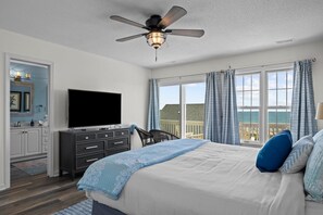 Une chambre à coucher comprenant un lit, un téléviseur, un ventilateur de plafond, une commode et une fenêtre avec des rideaux.