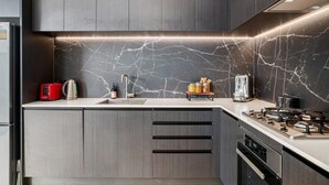 A modern kitchen with dark cabinetry, a marble backsplash, and a gas stove. - Nestled below the Remarkables (Jacks Point)