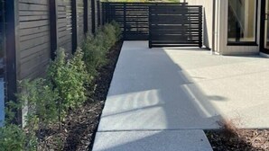 A modern building with a concrete pathway leading to a gated entrance, surrounded by a wooden fence and vegetation. - Nestled below the Remarkables (Jacks Point)