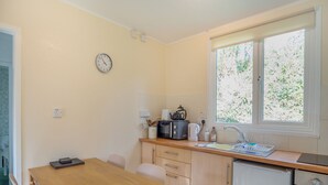 A compact kitchen with a wooden table, white chairs, a microwave, kettle, and a sink. - Comfortable log cabin offering self-catering in the heart of Cornwall. (Ruthernbridge, Nr Bodmin)