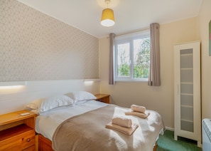 A hotel room with a bed, bedside tables, a window with curtains, a wardrobe, and a wall with a geometric pattern. - Comfortable log cabin offering self-catering in the heart of Cornwall. (Ruthernbridge, Nr Bodmin)