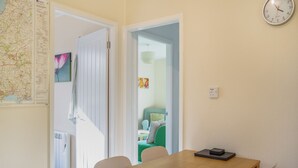 A room with a wooden table, chairs, a clock, a map, and a radiator. - Comfortable log cabin offering self-catering in the heart of Cornwall. (Ruthernbridge, Nr Bodmin)