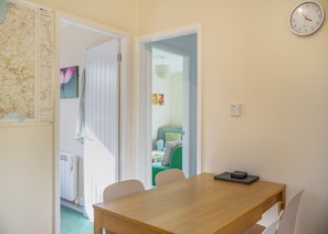 A room with a wooden table, chairs, a clock, a map, and a radiator. - Comfortable log cabin offering self-catering in the heart of Cornwall. (Ruthernbridge, Nr Bodmin)