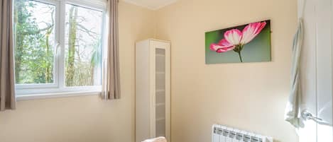 A bedroom with a bed, a radiator, a window with curtains, and a painting of a flower.