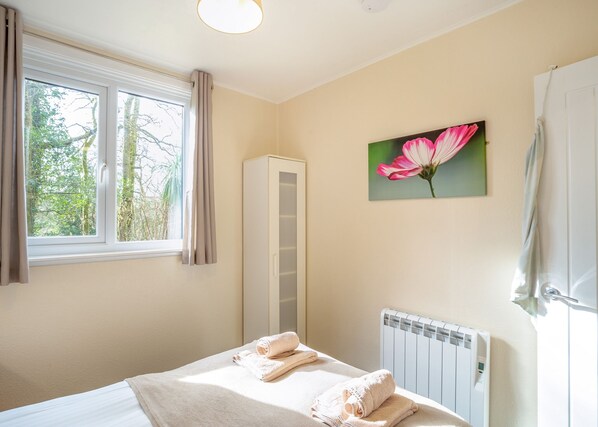 A bedroom with a bed, a radiator, a window with curtains, and a painting of a flower.