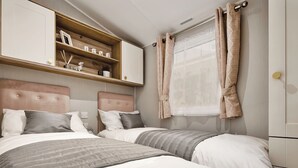 Un dormitorio con dos camas, una estantería con objetos, una ventana con cortinas y un armario.