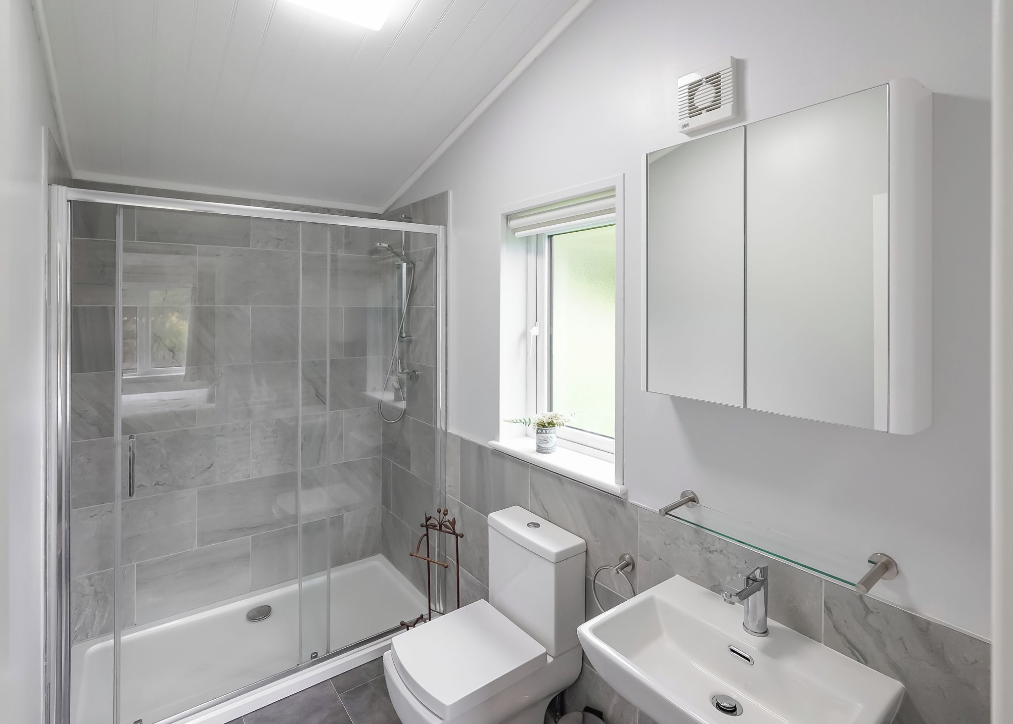 A modern bathroom with a glass-enclosed shower, a toilet, and two sinks.