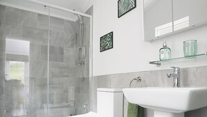 Ein modernes Badezimmer mit Duschkabine aus Glas, einer weißen Toilette, einem Waschbecken mit grünem Handtuch und Wanddekoration.