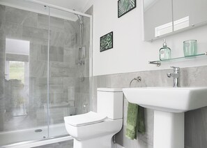 A modern bathroom with a glass shower enclosure, a white toilet, a sink with a green towel, and decorative wall art.