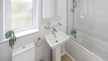 A modern bathroom with a white sink, a glass shower enclosure, a toilet, and a window with a plant.