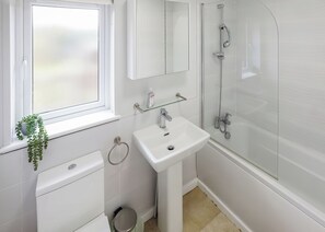 Une salle de bain moderne avec un lavabo blanc, une douche en verre, des toilettes et une fenêtre agrémentée d’une plante.