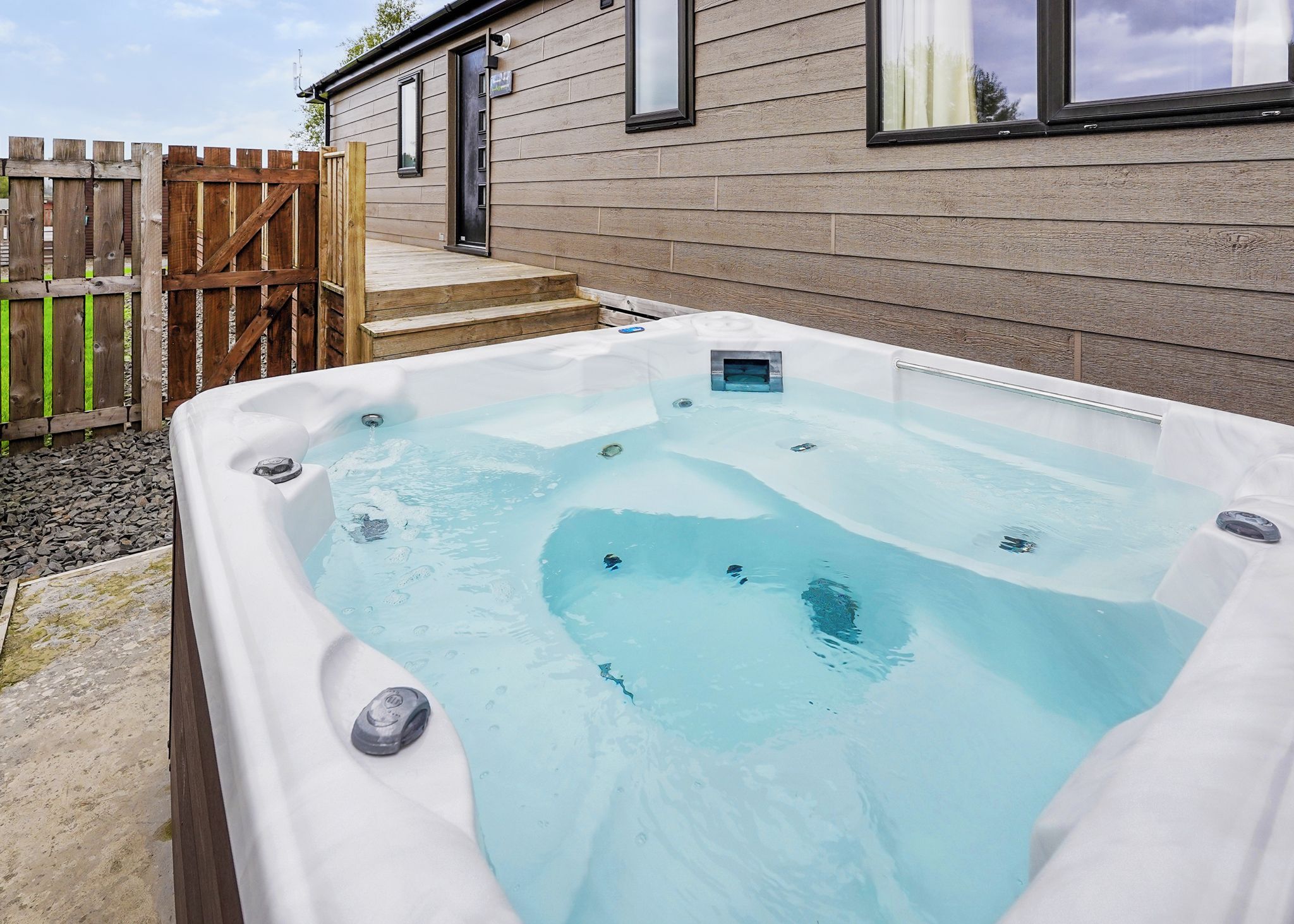 A hot tub in a backyard with a wooden fence and a house in the background.