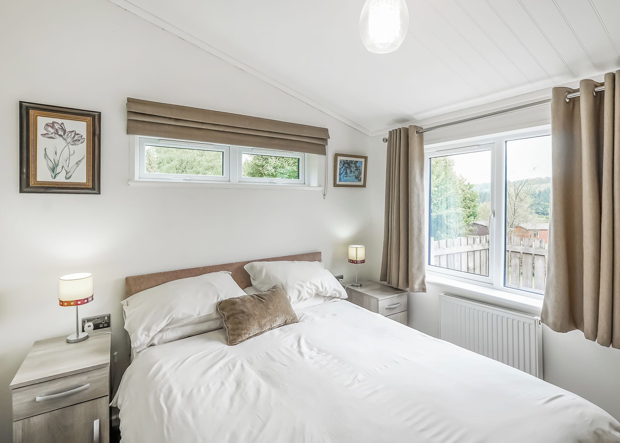 A bedroom with a bed, bedside tables, a window with curtains, and wall-mounted artwork.