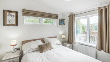 A bedroom with a bed, bedside tables, a window with curtains, and wall-mounted artwork.