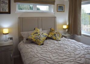 A bedroom with a large bed, two bedside lamps, a window with curtains, and a headboard.
