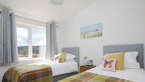 Ein Schlafzimmer mit zwei Betten, einem Fenster mit Vorhängen, einem Nachttisch mit Lampe und einem Bild an der Wand.