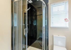 A glass-enclosed shower with a white toilet and blinds on a window. - New in 2017. Modern and contemporary 14ft-wide lodge style holiday home. (Hawes,)