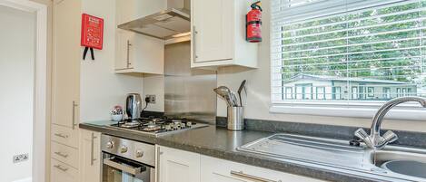 A modern kitchen with stainless steel appliances, a window with blinds, and a fire extinguisher mounted on the wall.