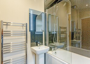 A bathroom with a glass-enclosed shower, a white sink, and a glass-enclosed mirror with lights.