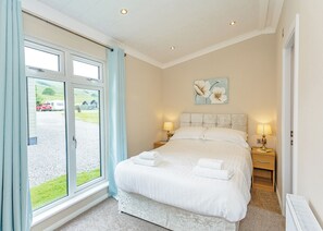 A bedroom with a large bed, two bedside tables with lamps, a window with curtains, and a painting on the wall.
