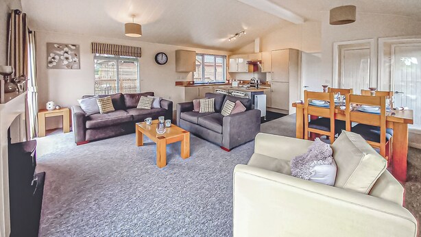 A living room with two sofas, a coffee table, and a dining area with a table set for four. - Luxury lodge with one double with en suite shower and one twin. (Thirsk)