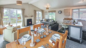 A dining area with a table set for four, a sofa, a fireplace, and a kitchen in the background. - Luxury lodge with one double with en suite shower and one twin. (Thirsk)