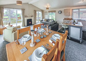A dining area with a table set for four, a sofa, a fireplace, and a kitchen in the background.