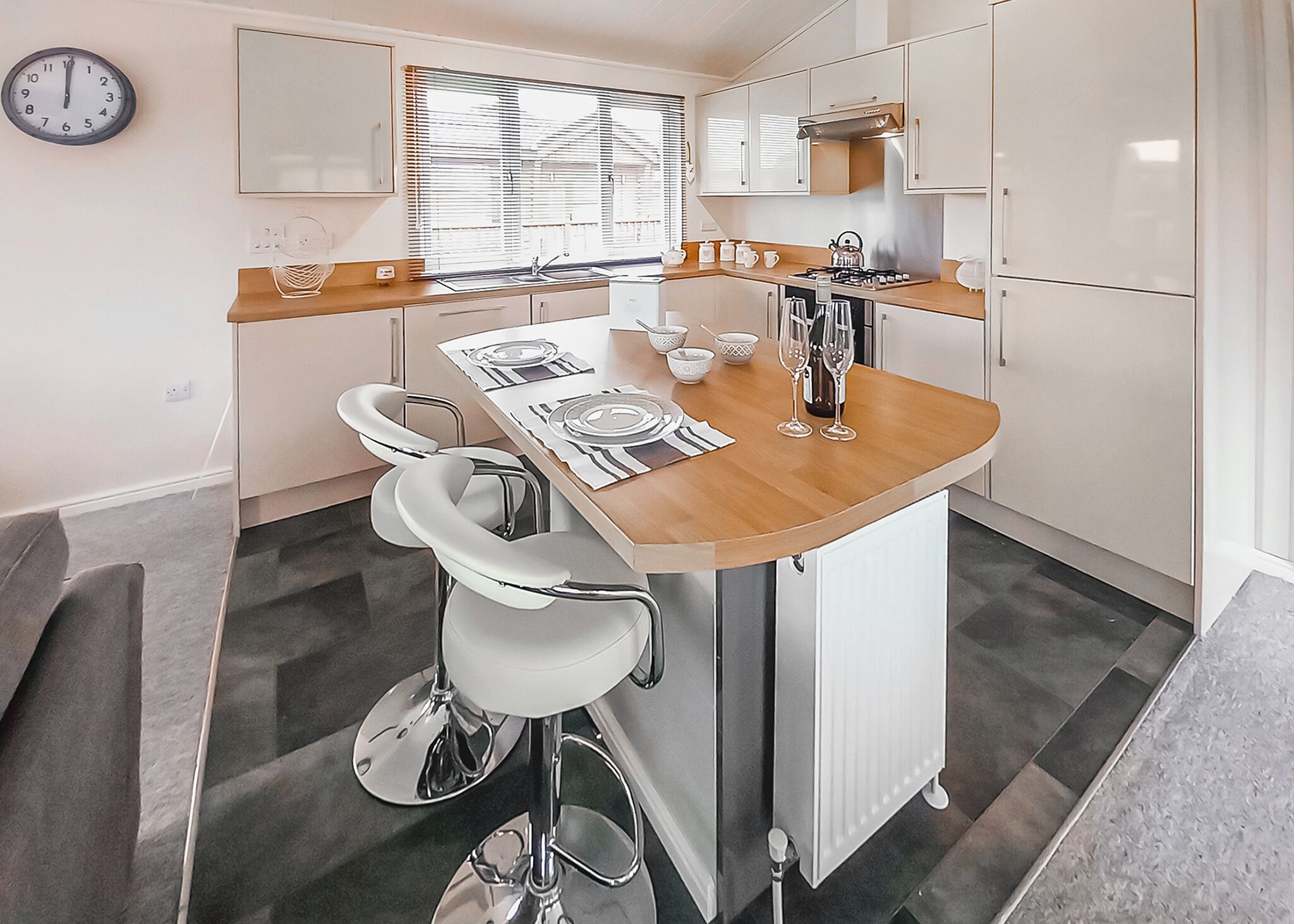 A compact kitchen with a central island, a sink, and a stove. There are two bar stools and a clock on the wall.